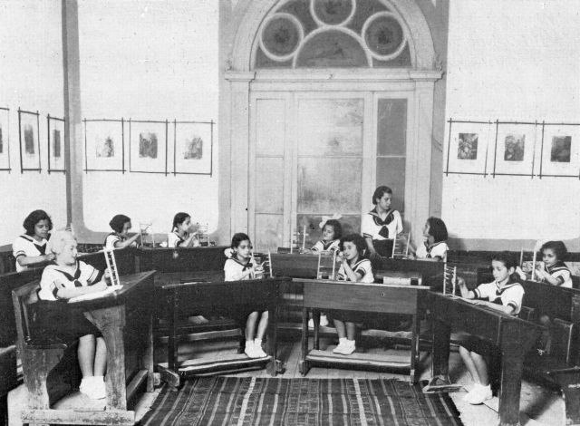 Μάθημα Αριθμητικής στην Α΄ τάξη τού Αρσακείου Δημοτικού Πατρών με χρήση αριθμητηρίου. Η τάξη είναι διακοσμημένη με τις εικόνες από την Παλαιά και την Καινή Διαθήκη τού οίκου Hachette. Η διάταξη των θρανίων είναι πρωτοποριακή για την εποχή. E031a